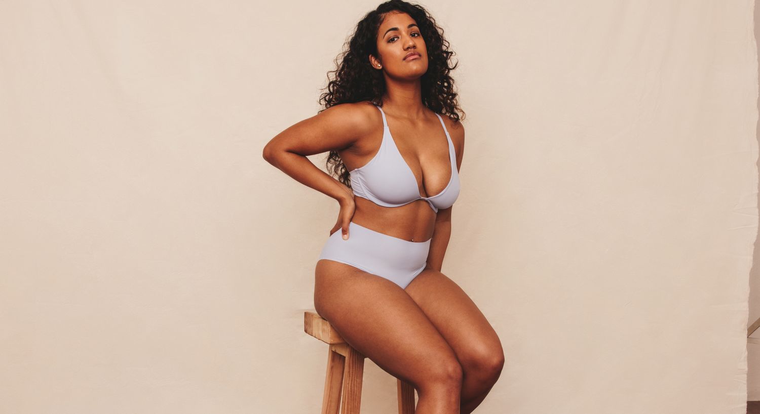 Avon liposuction model posing in light blue lingerie seated on stool.